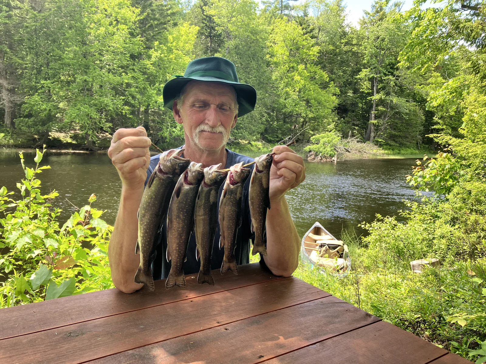 Client holding a stringer of brook trout beside a Maine river