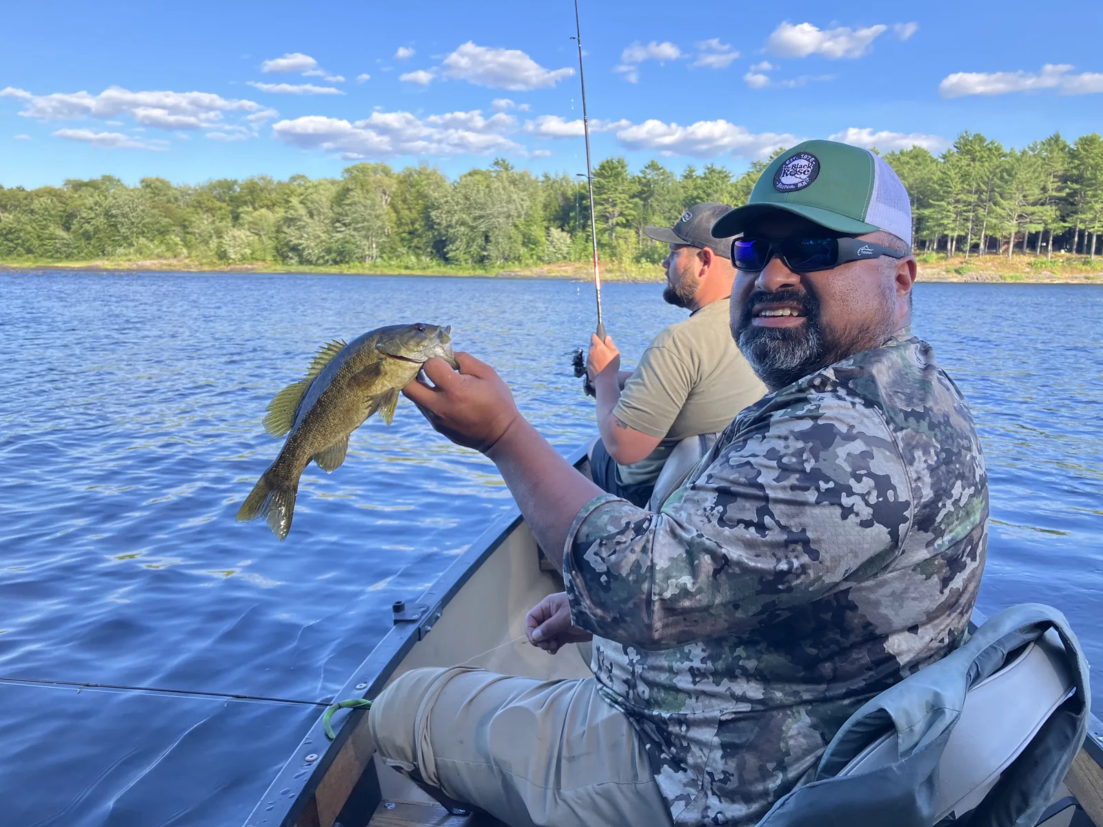 Client holding a fish while seated in a canoe on a Maine lake