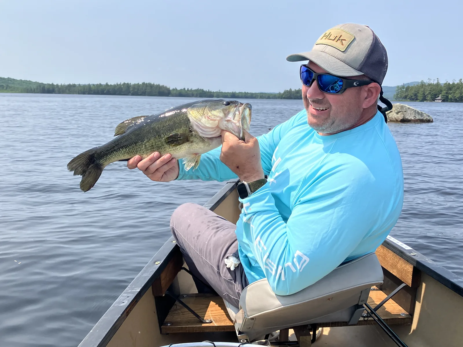 Client holding a largemouth bass from a canoe on a Maine lake