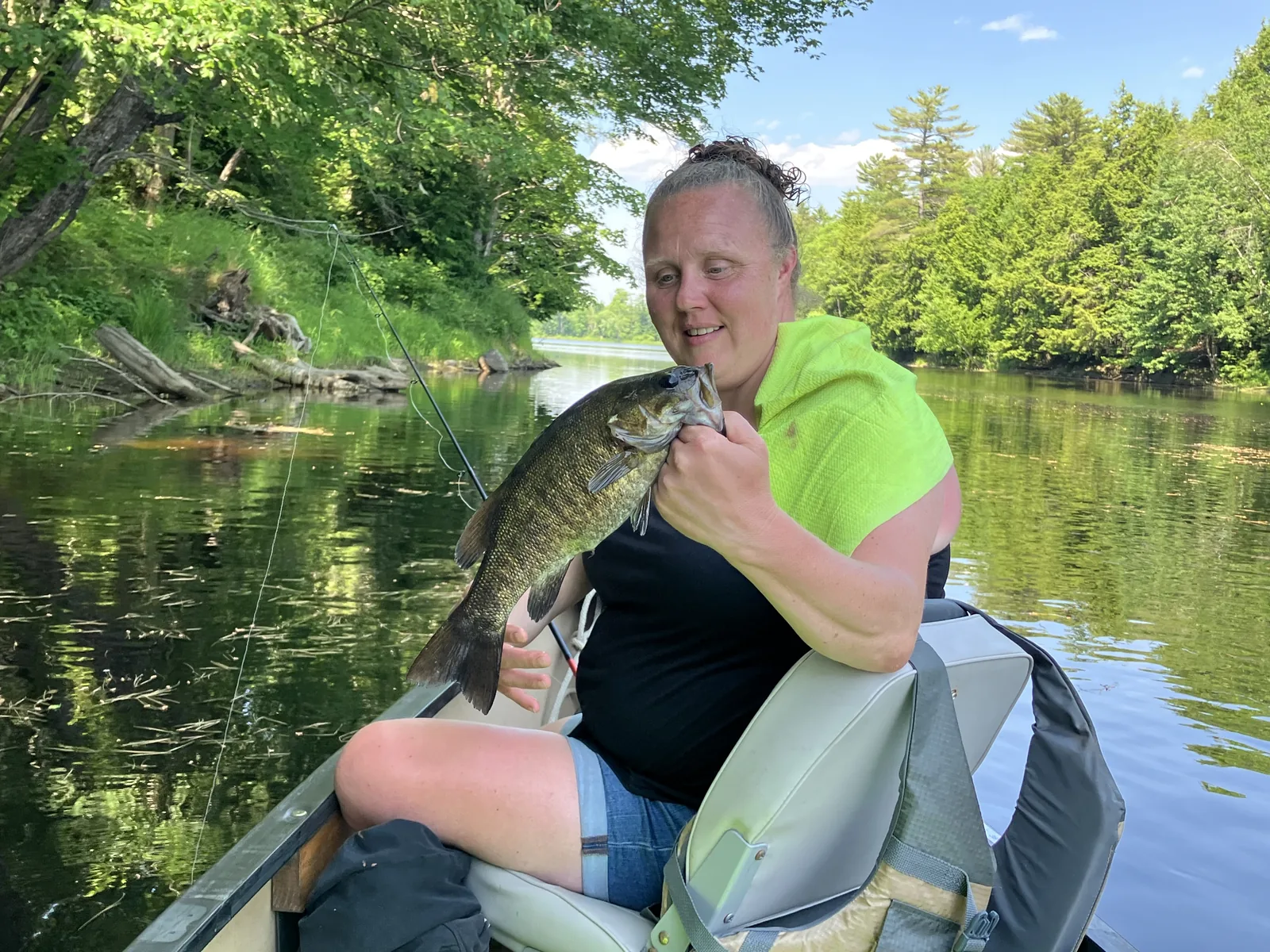 Client holding a smallmouth bass from a canoe on a Maine river