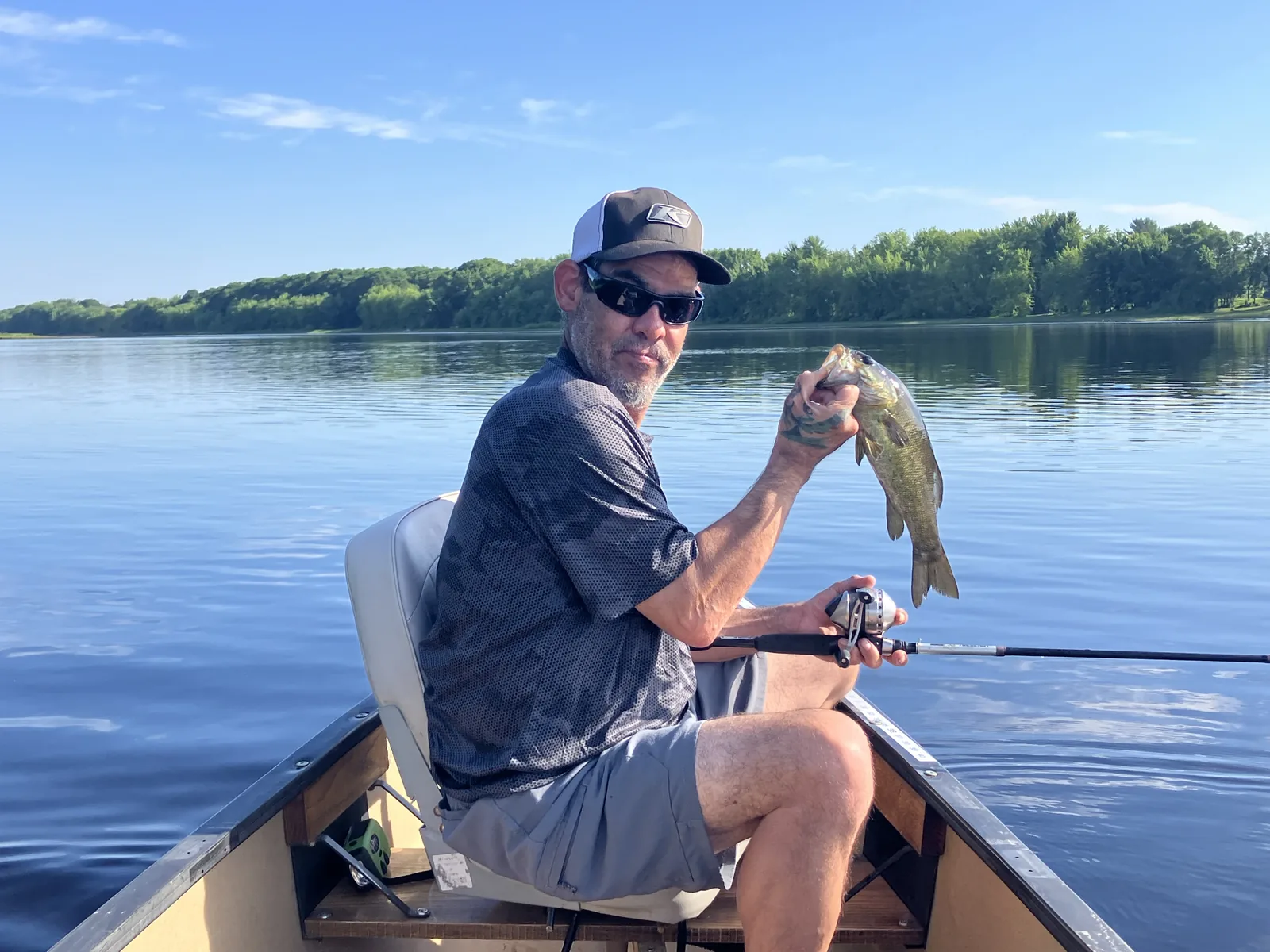 Client holding a smallmouth bass while fishing from a canoe on calm water