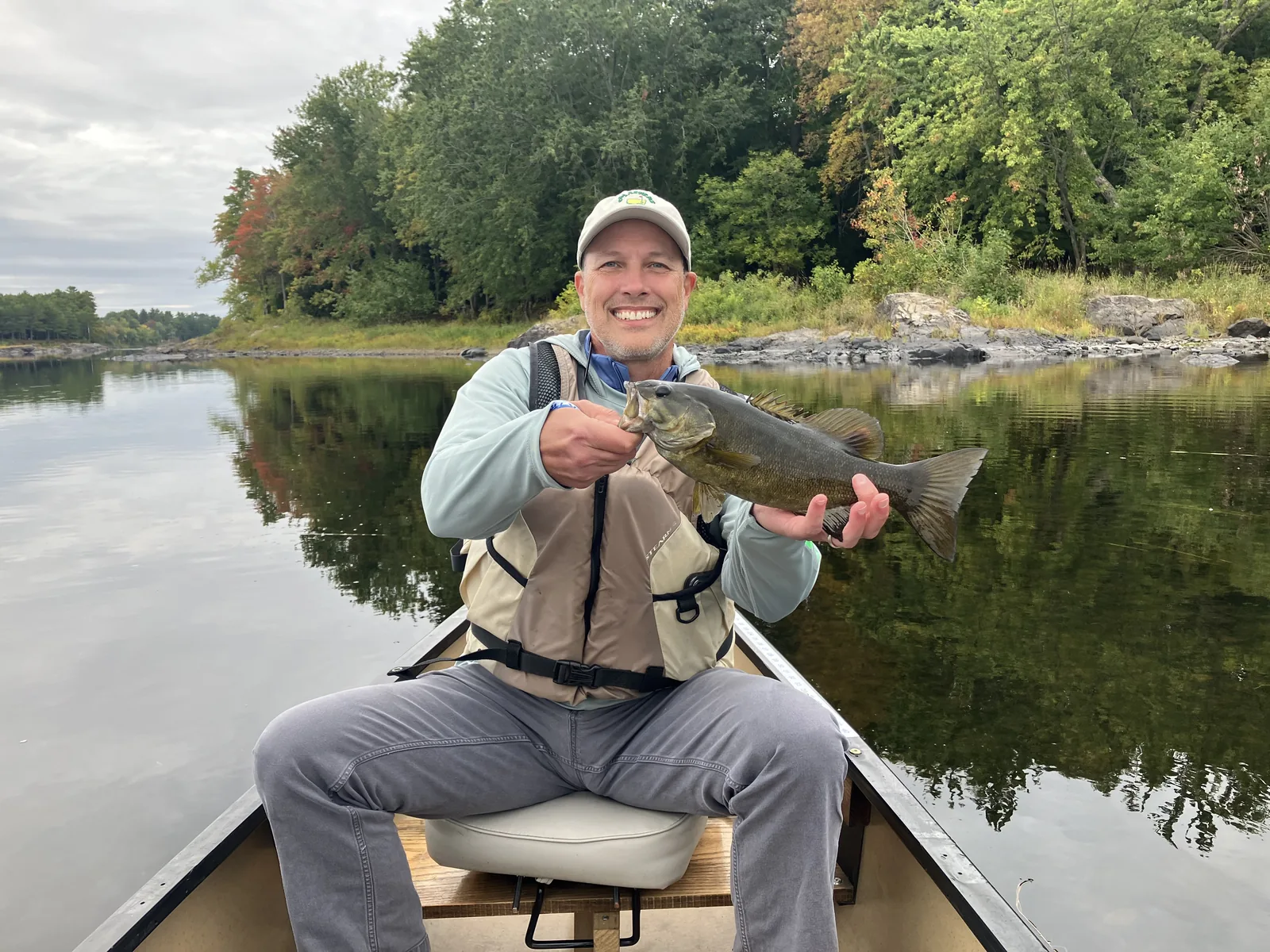 Client holding a smallmouth bass during a guided fishing trip on calm water