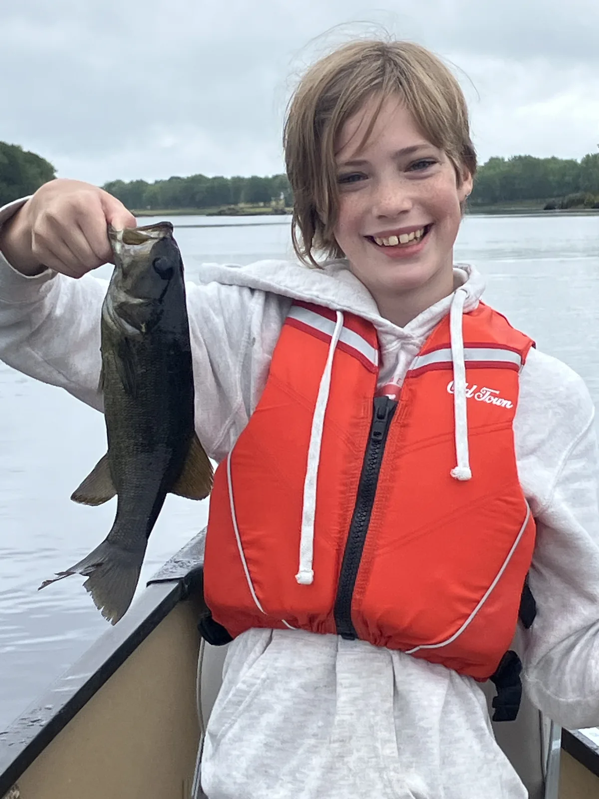 Young angler smiling with a smallmouth bass during a guided fishing trip