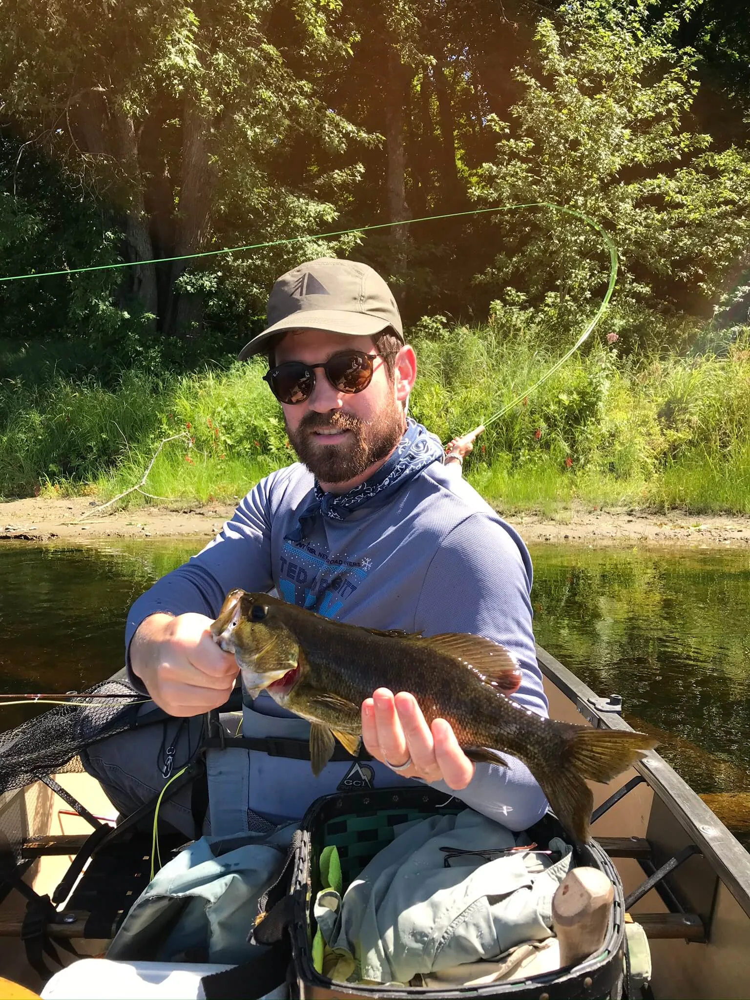 Client holding a smallmouth bass while fly fishing from a canoe
