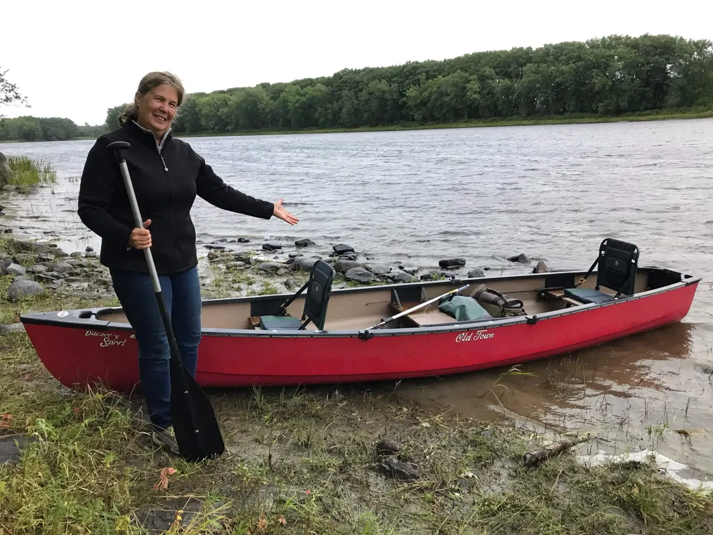 Client standing beside a canoe at a Maine river landing