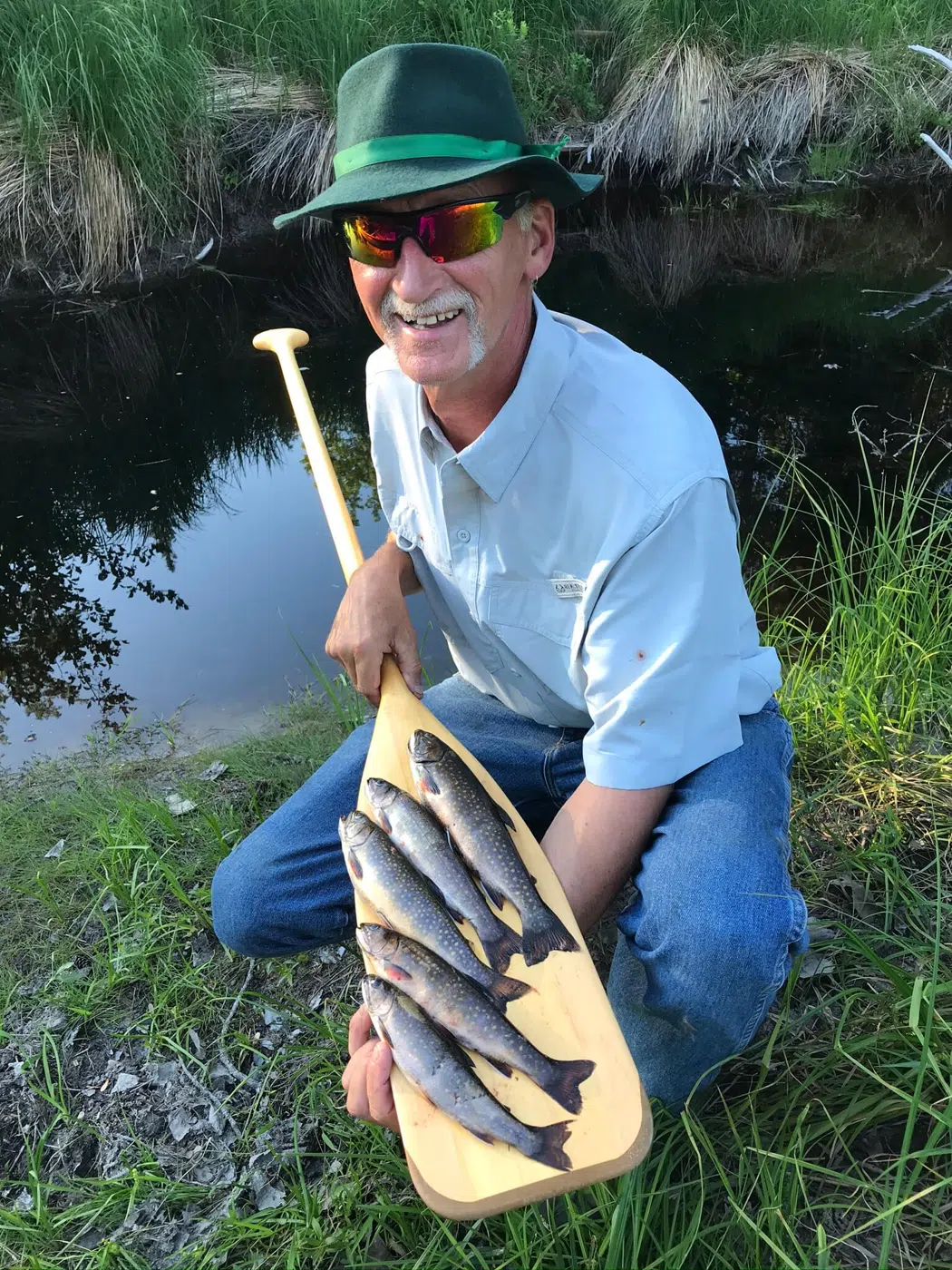 Client holding a stringer of fish beside a Maine river