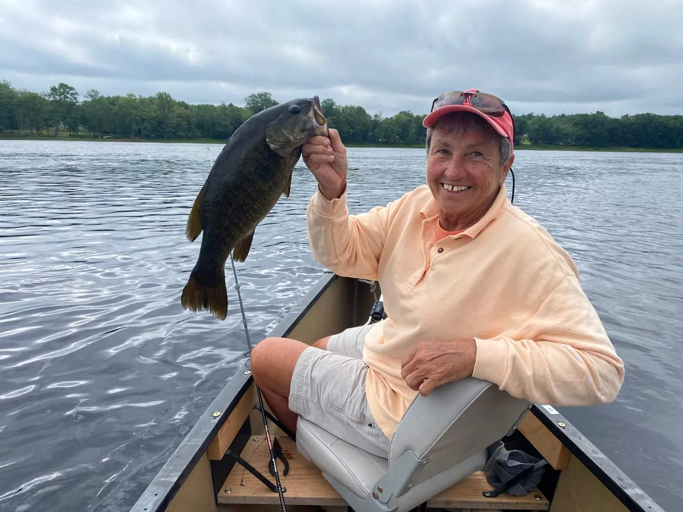 Client holding a smallmouth bass from a canoe on a Maine lake