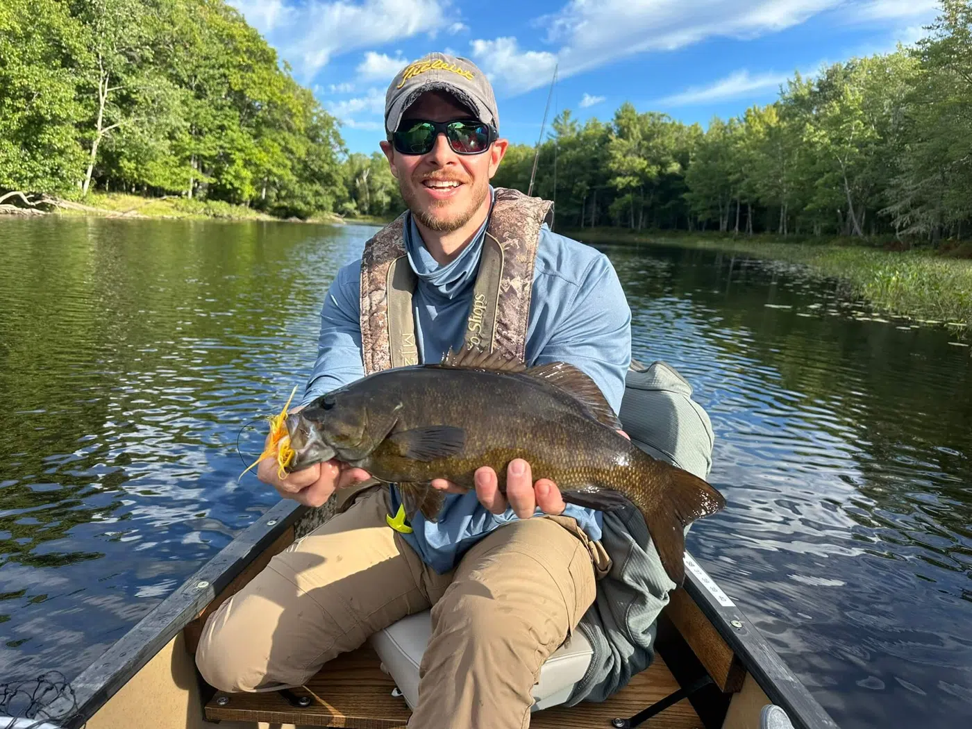 Client holding a large bass from a canoe on a Maine river