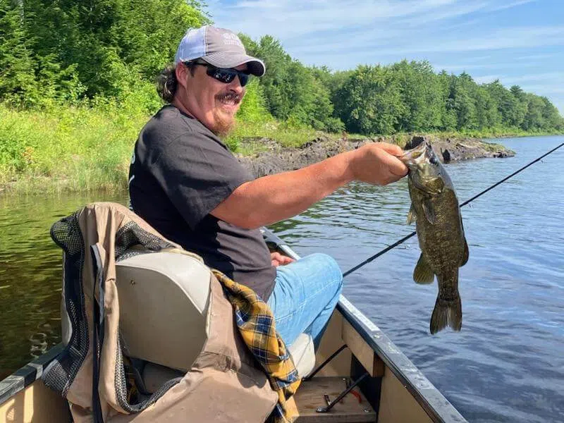 Client holding a bass while fishing from a canoe