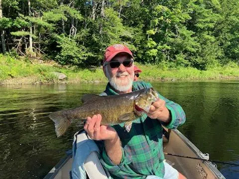 Client holding a smallmouth bass from a canoe on a Maine river