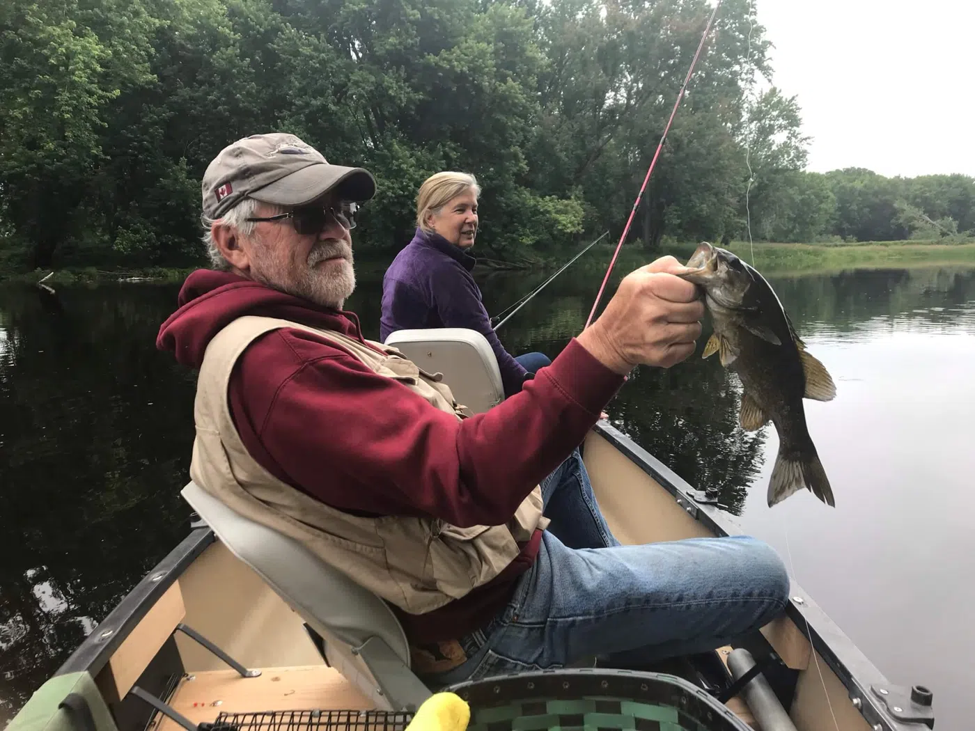 Client holding a bass while fishing from a canoe