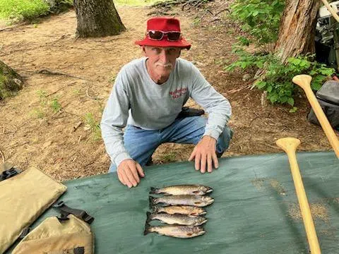 Client displaying fish on a table beside a Maine river