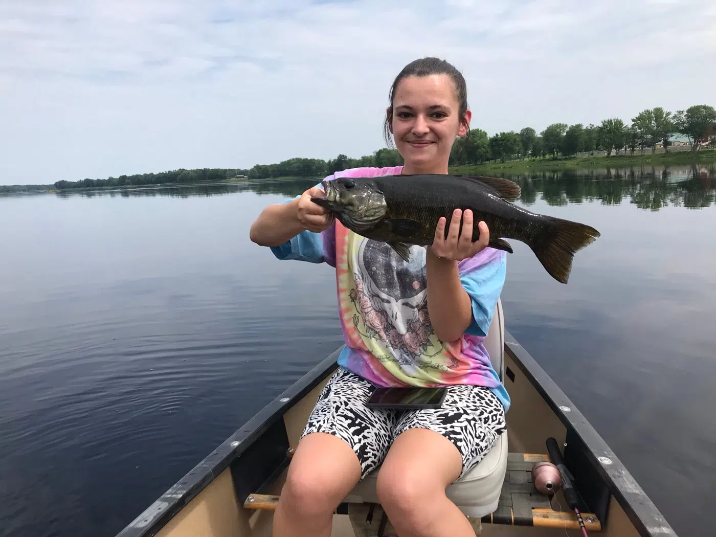 Client holding a smallmouth bass from a canoe on calm water