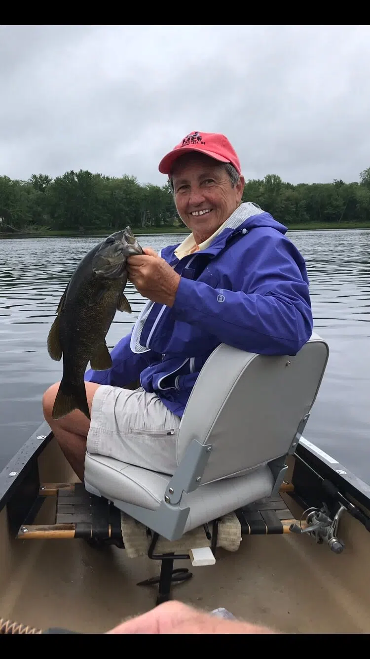 Client holding a bass while fishing from a canoe