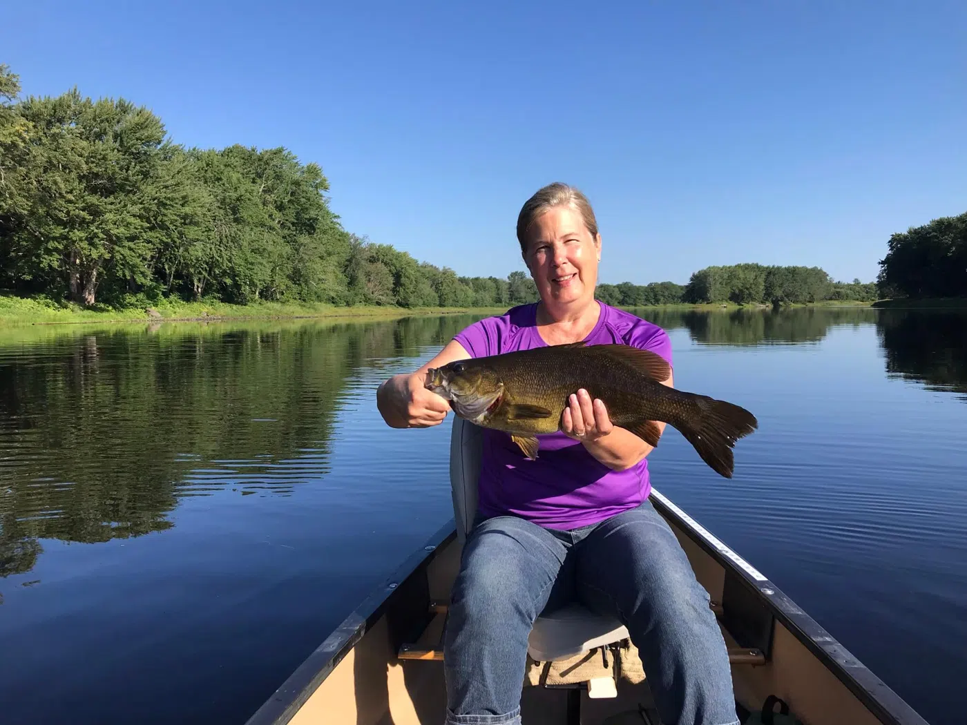 Client holding a smallmouth bass from a canoe on a sunny day